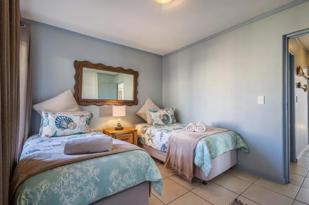Twin bedroom with coastal-themed bedding and wooden framed mirror