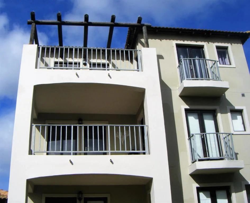 Modern white apartment building with multiple balconies and metal railings against blue sky