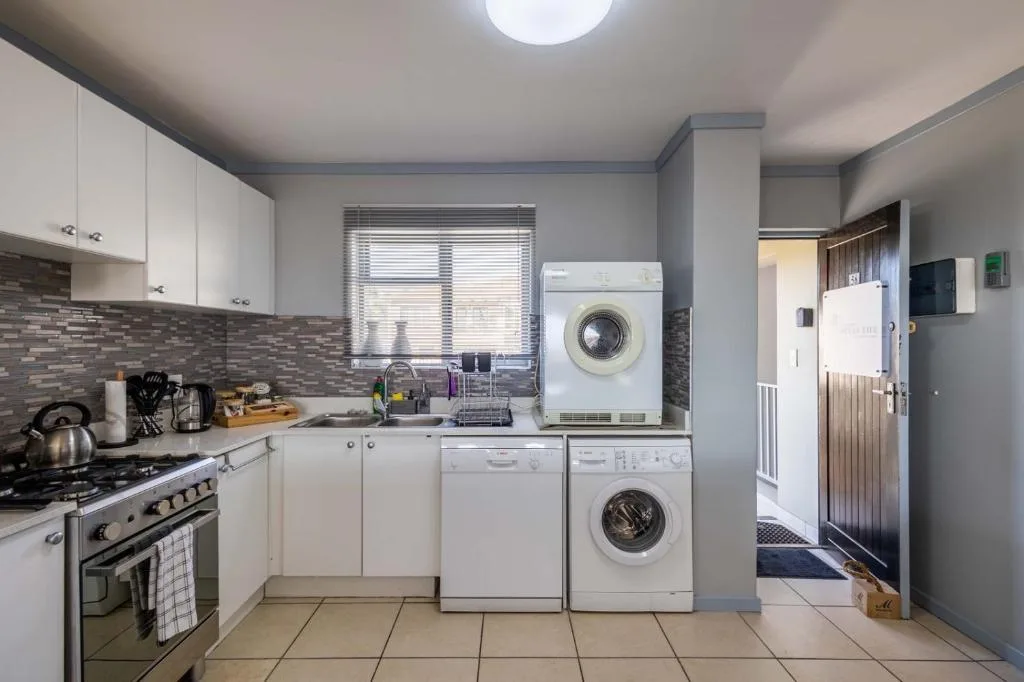 Modern kitchen with white cabinetry, gas stove, and stacked washing machines