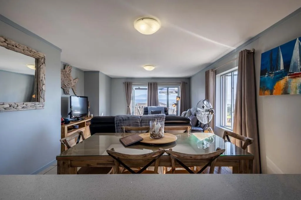 Open-plan lounge with sofa, TV, and ocean views through glass doors