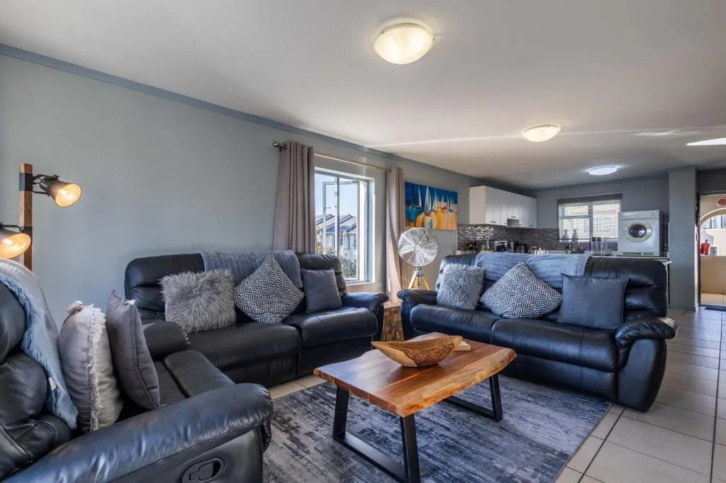 Modern lounge with black leather sofas, wooden coffee table, and open kitchen view