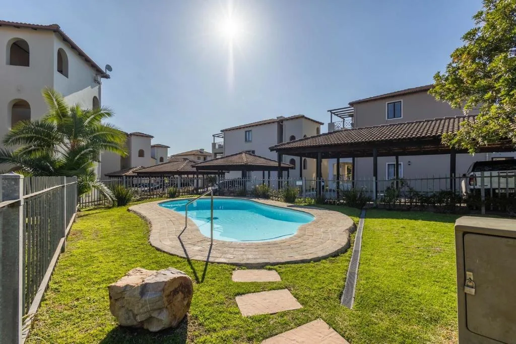 Sparkling blue kidney-shaped swimming pool with shaded pergola and manicured lawn