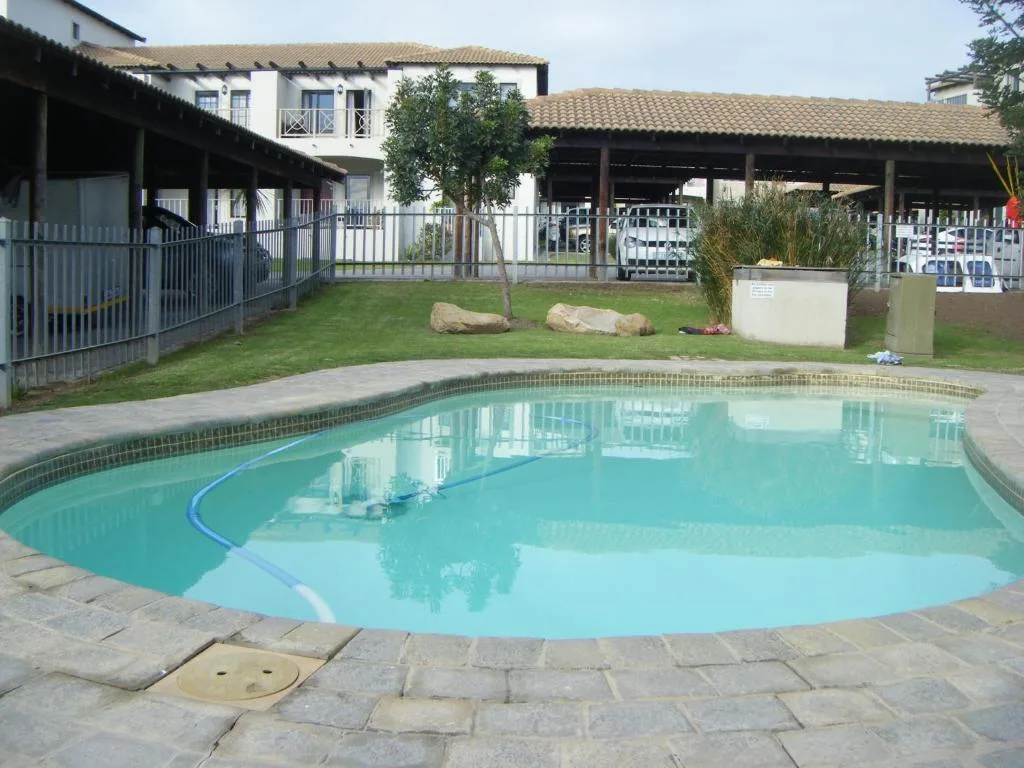 Turquoise swimming pool with stone paving and property buildings behind