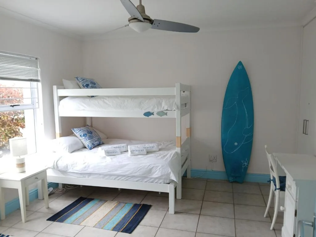 Bright bedroom with white bunk beds and coastal decor including surfboard