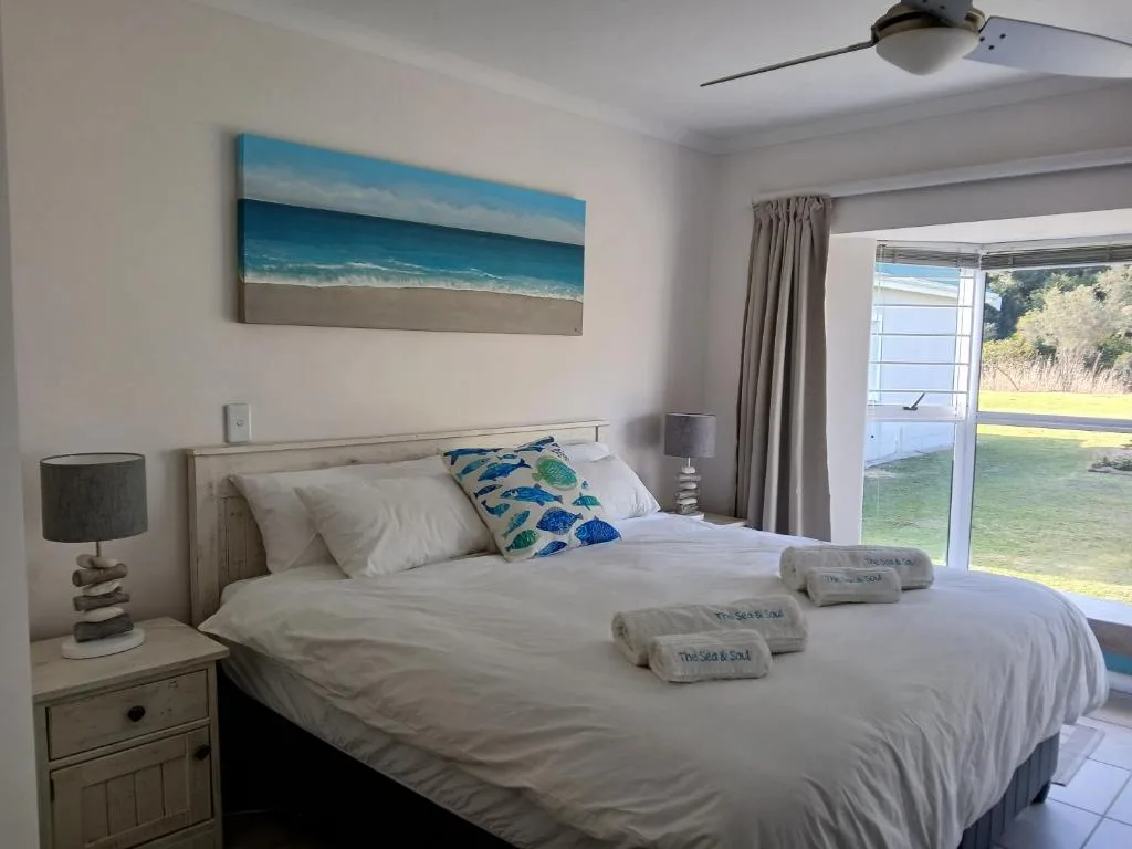 Bright bedroom with queen bed, ocean artwork, and garden views through glass doors