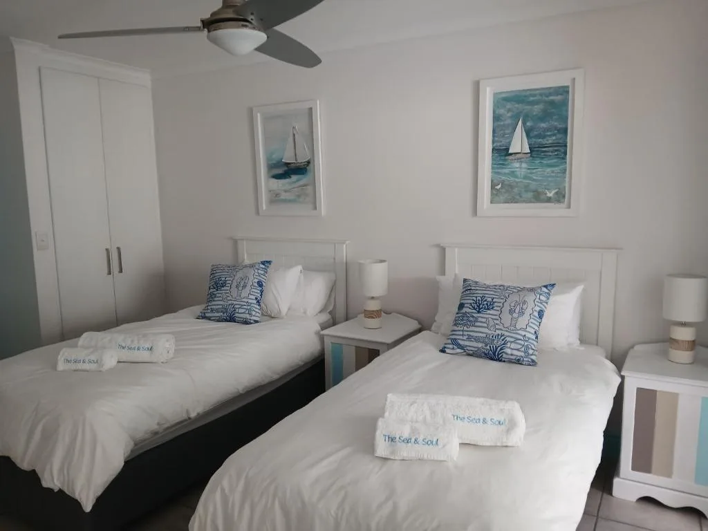 Twin bedroom with white bedding, nautical artwork, and ceiling fan