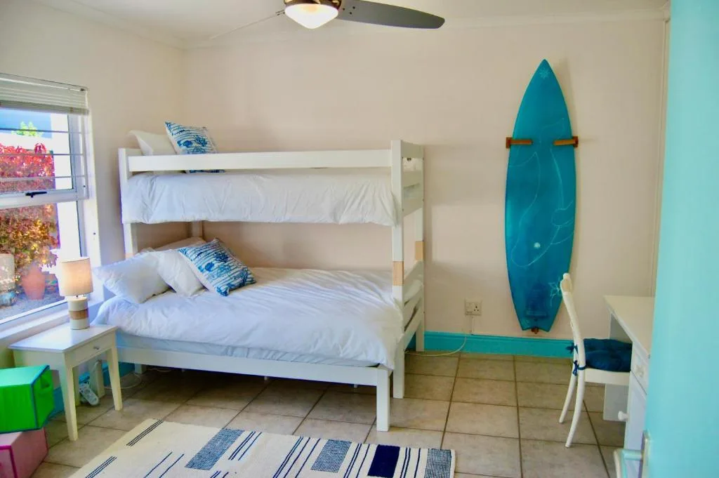 Bright bedroom with white bunk beds and turquoise surfboard wall decoration