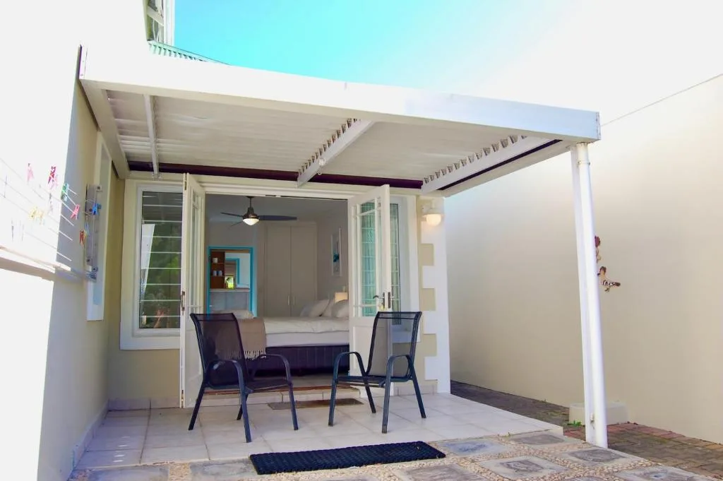 Covered patio with white pergola, two chairs, and bedroom view beyond