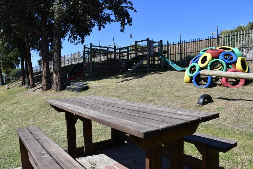 Picnic table with colorful playground equipment and wooden structures in background