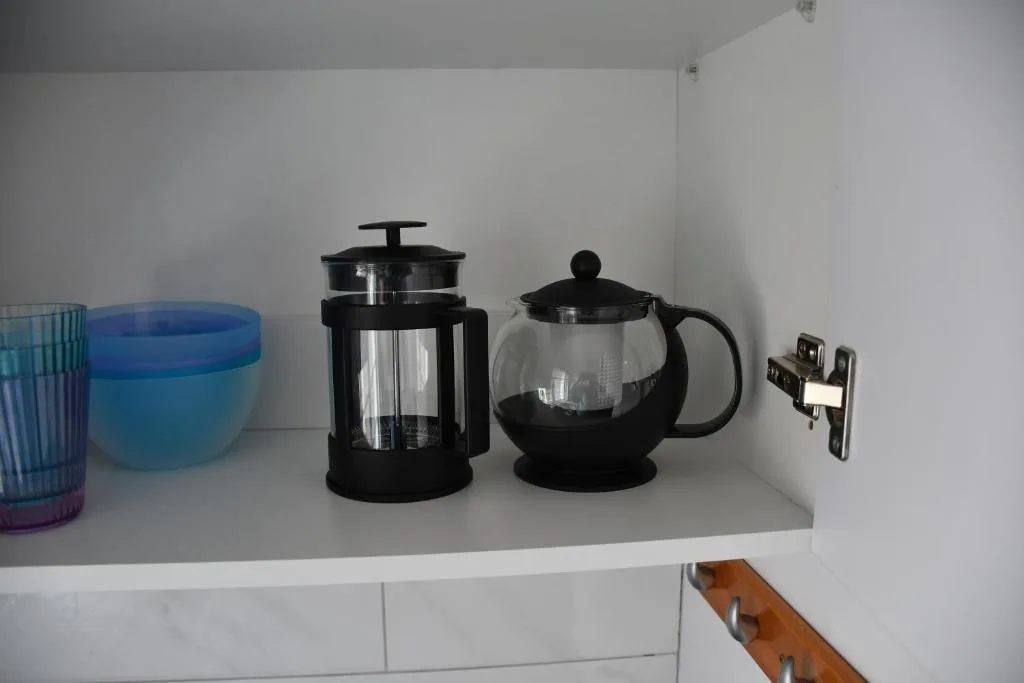 Kitchen shelf displaying coffee press, teapot, and glass cups
