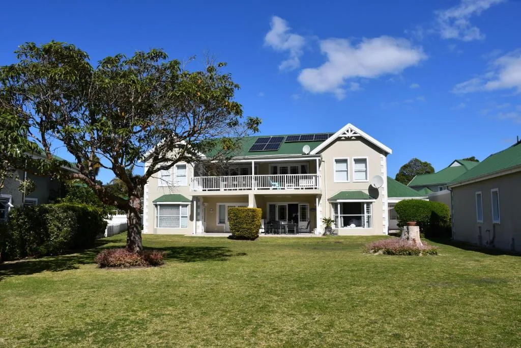 White two-story villa with green roof and solar panels, manicured lawn