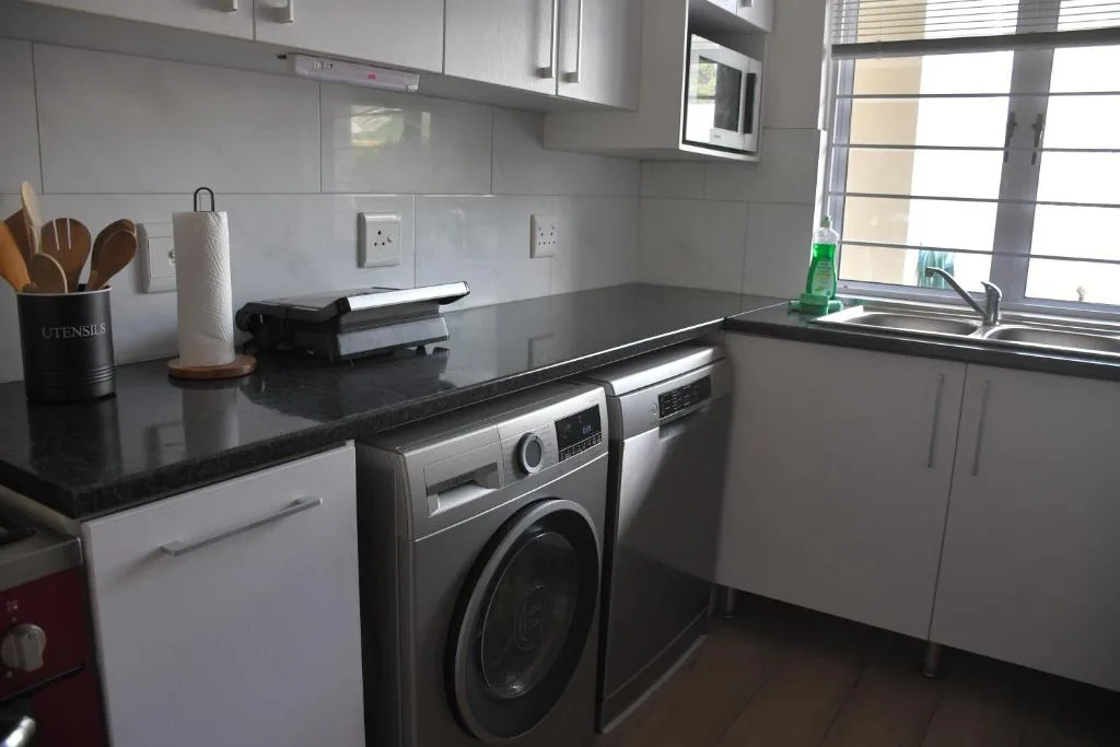 Modern kitchen with white cabinetry, black countertops, and stainless steel appliances