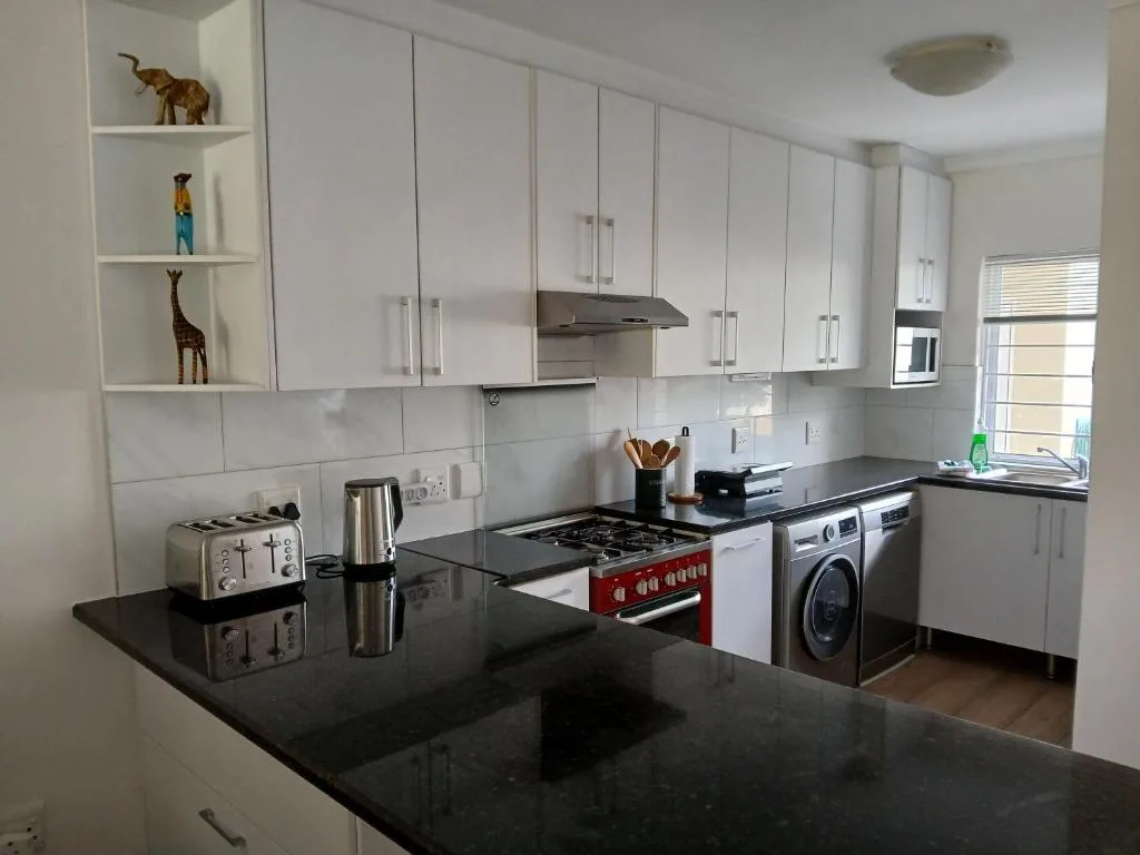 Modern kitchen with white cabinetry, black countertops, and red gas range
