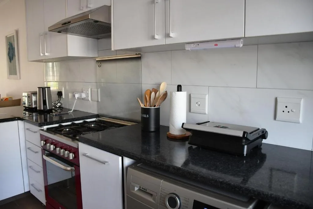 Modern kitchen with white cabinets, black countertops, red oven, and stainless steel appliances