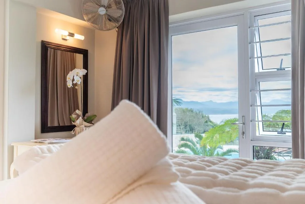 Bright bedroom with bed, mirror, fan, and lagoon view through doors