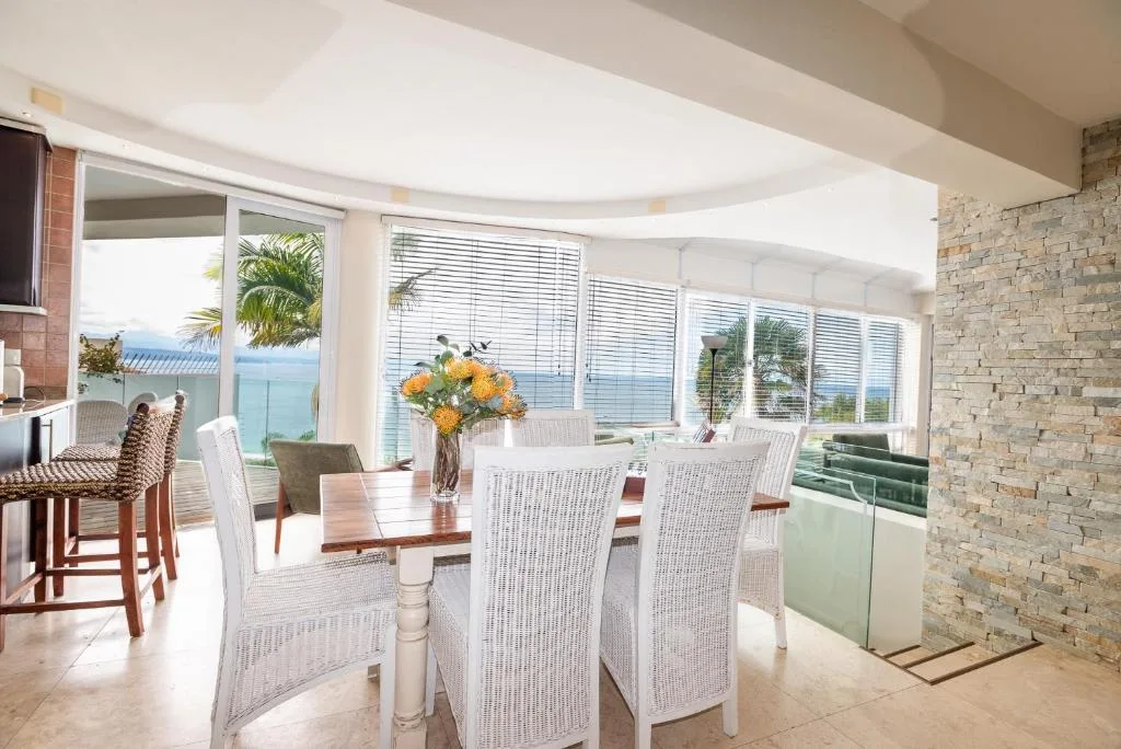 Bright dining area with wooden table, white wicker chairs, ocean views beyond