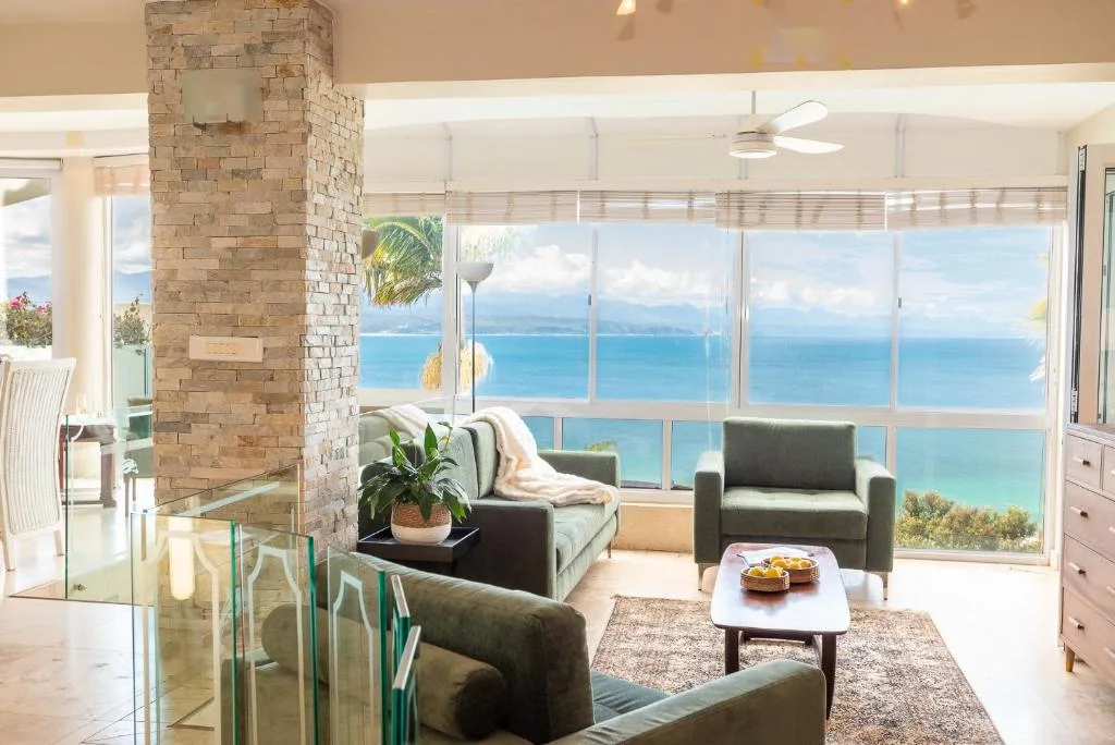 Modern lounge with ocean views through floor-to-ceiling windows and stone fireplace