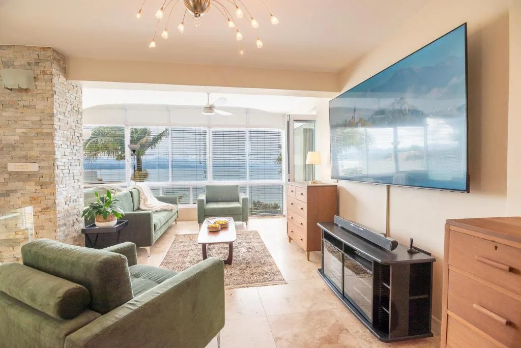 Modern lounge with green armchairs, TV, and ocean views through large windows