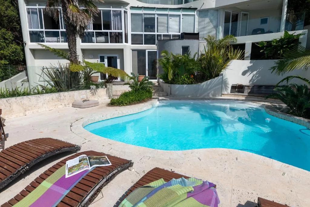 Bright turquoise swimming pool with loungers and modern white building