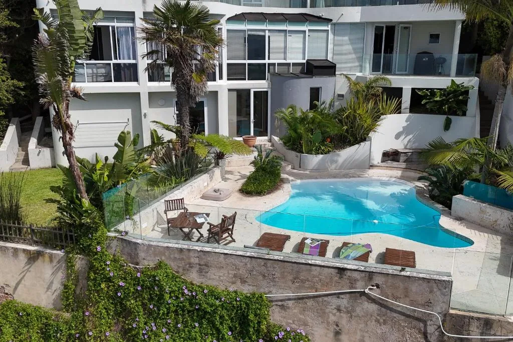 Sparkling blue swimming pool surrounded by tropical plants and lounge chairs