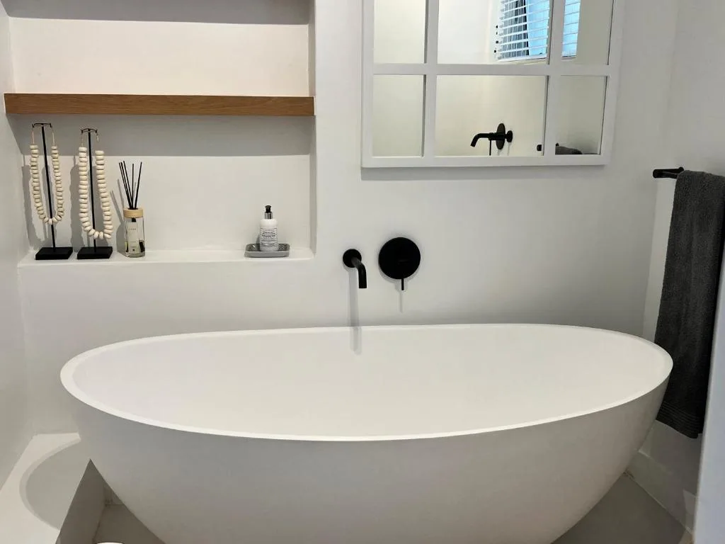 Modern freestanding white bathtub with black fixtures and shelving
