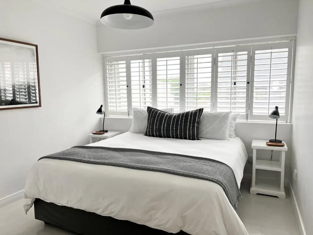 Bright modern bedroom with queen bed, white bedding, and large shuttered windows