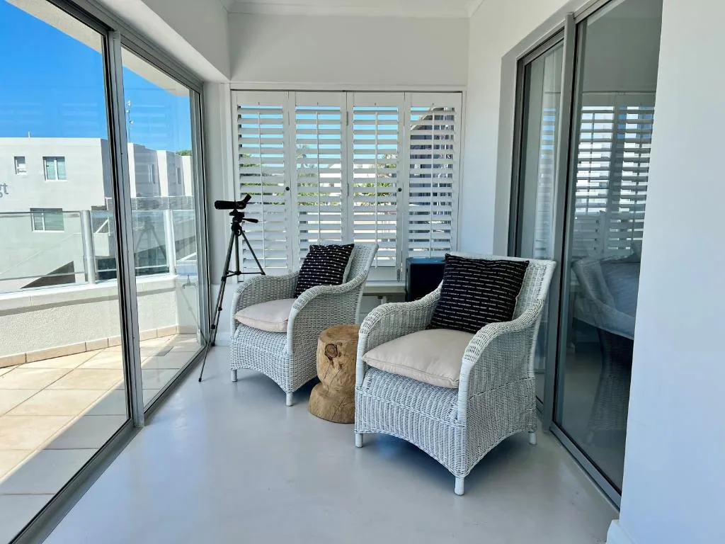 Modern covered balcony with wicker chairs and ocean views through shutters