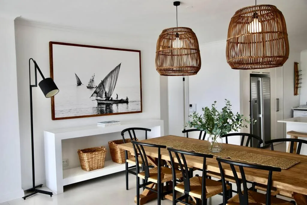 Dining area with wooden table, black chairs, and rattan pendant lights overhead