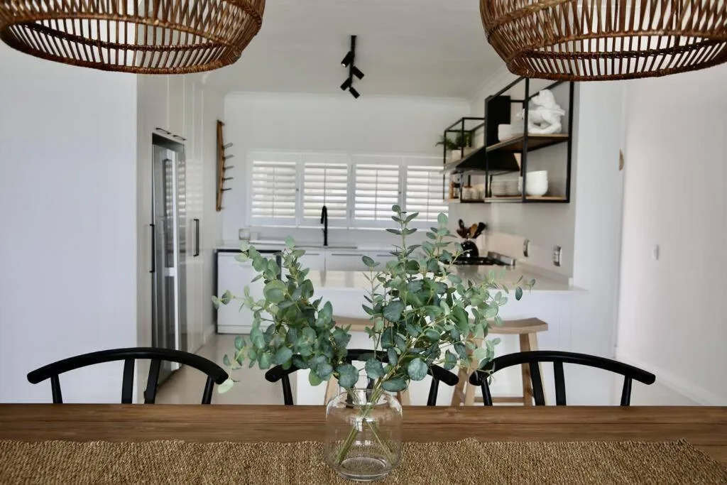 Modern dining area with wooden table, black chairs, and kitchen view beyond