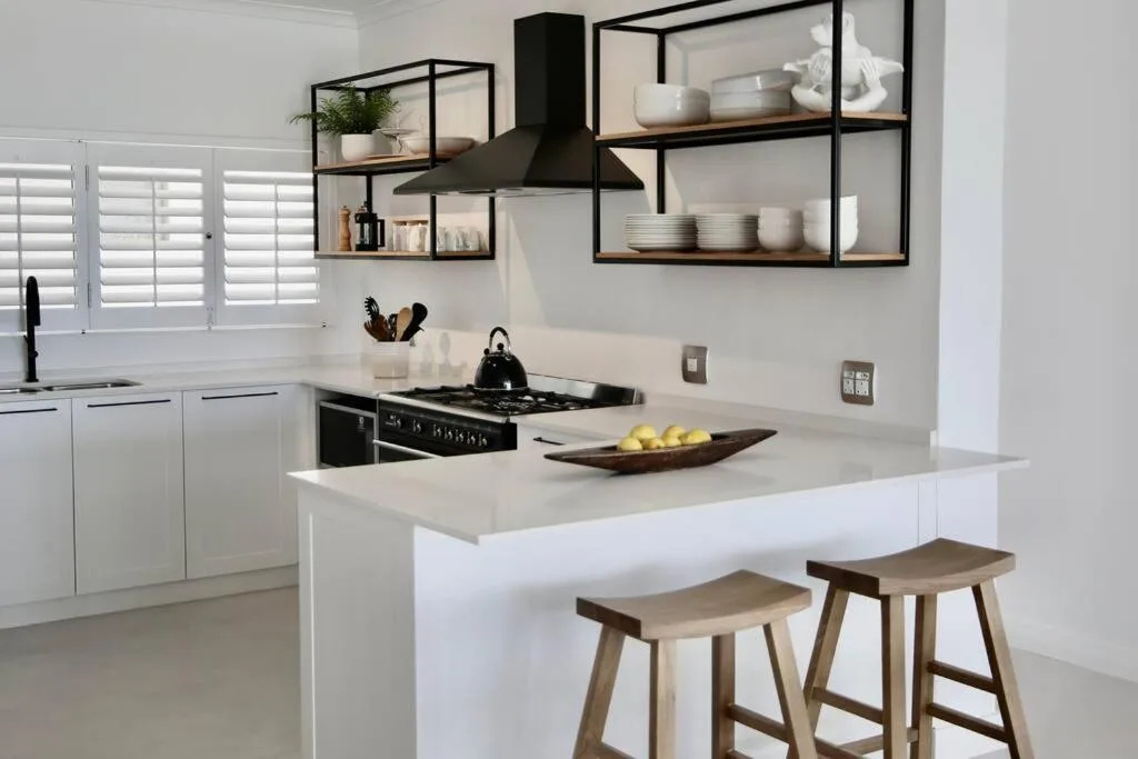 Modern white kitchen with black gas stove, open shelving, and island seating