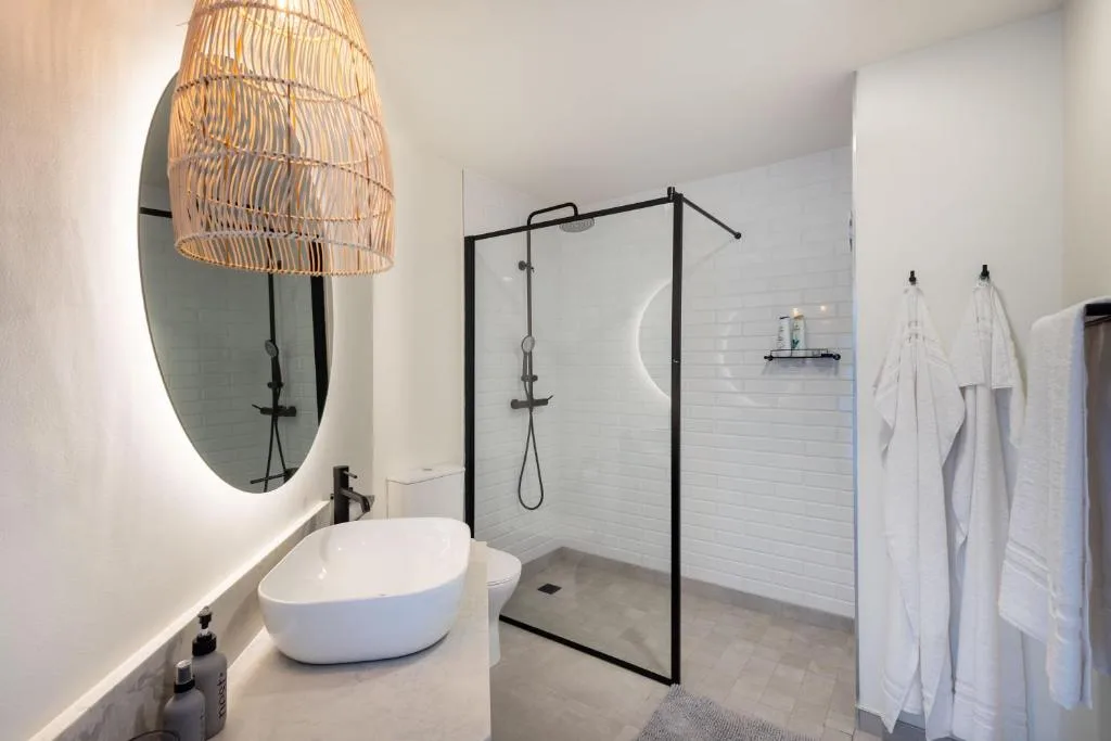 Modern bathroom with round vessel sink, illuminated mirror, and walk-in shower