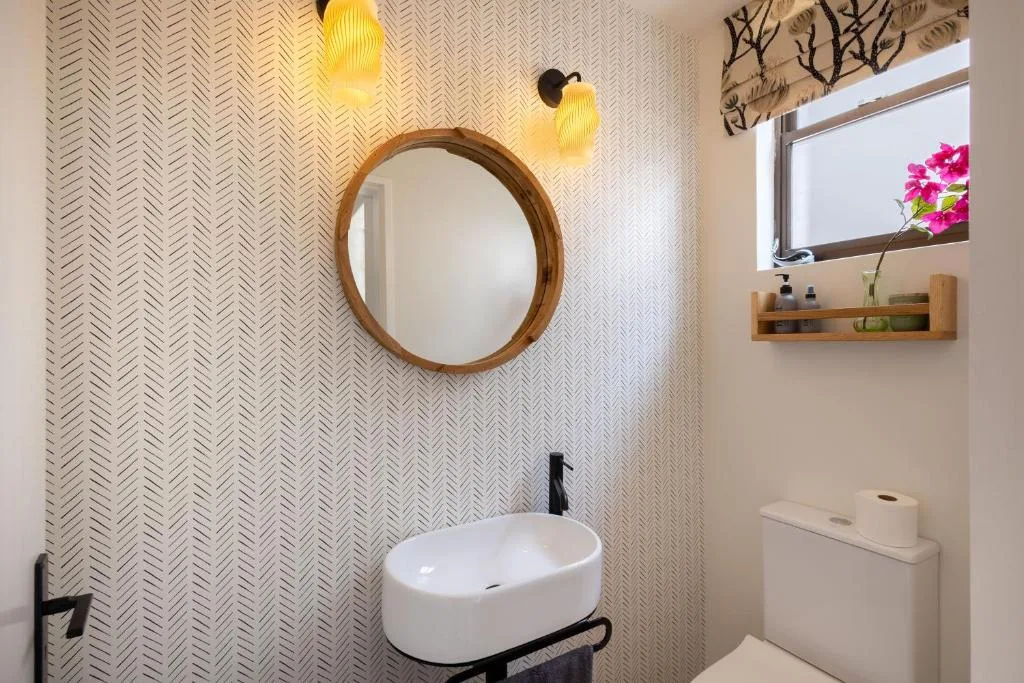 Modern bathroom with round wooden mirror, white vanity sink, and decorative lighting