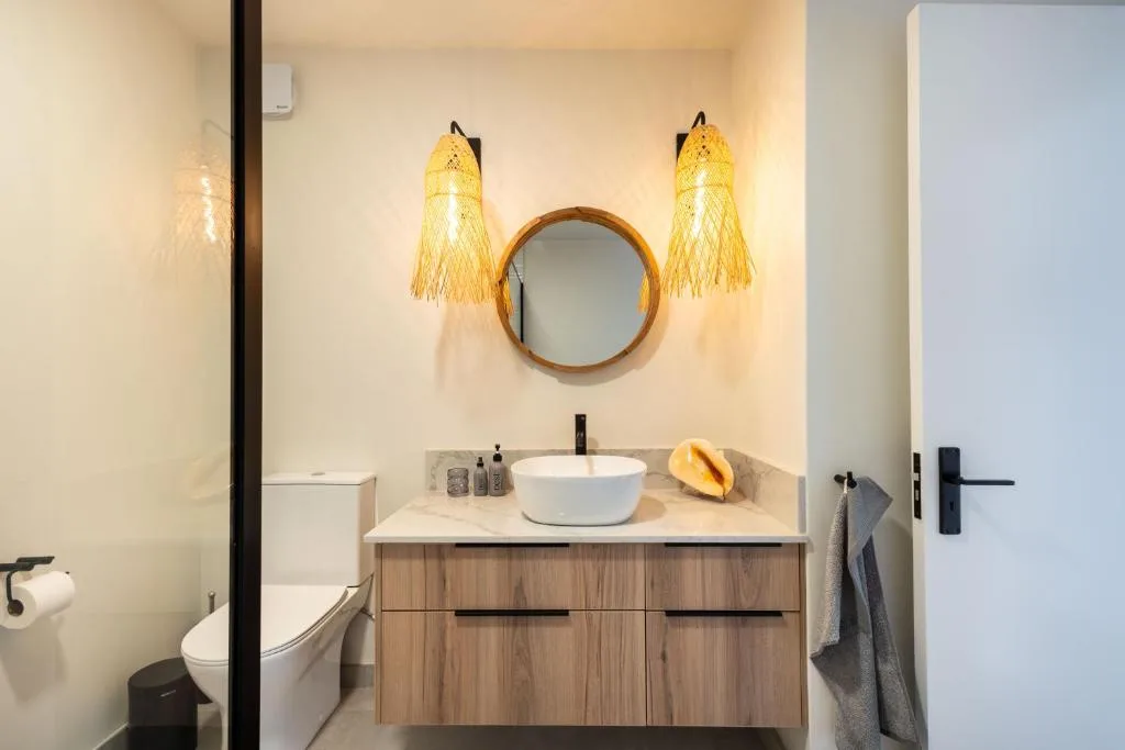 Modern bathroom with round mirror, white vessel sink, and woven pendant lights