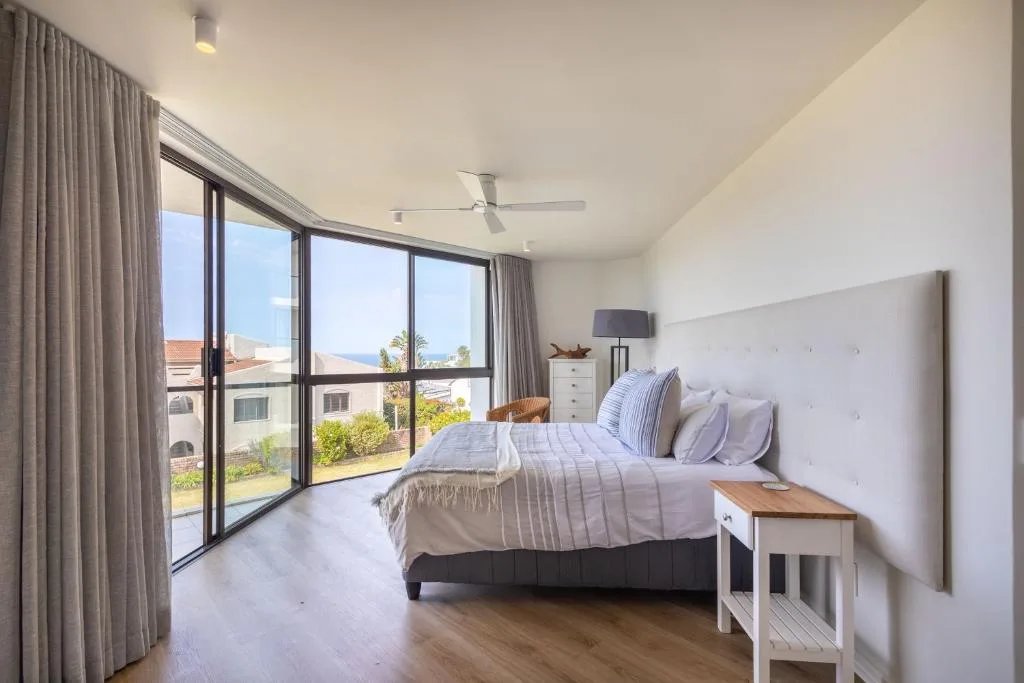 Bright bedroom with double bed, large windows overlooking coastal landscape