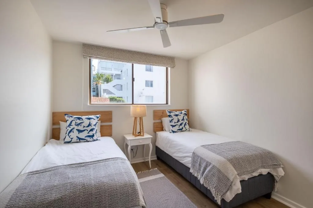 Twin bedroom with white bedding, navy patterned pillows, and ceiling fan