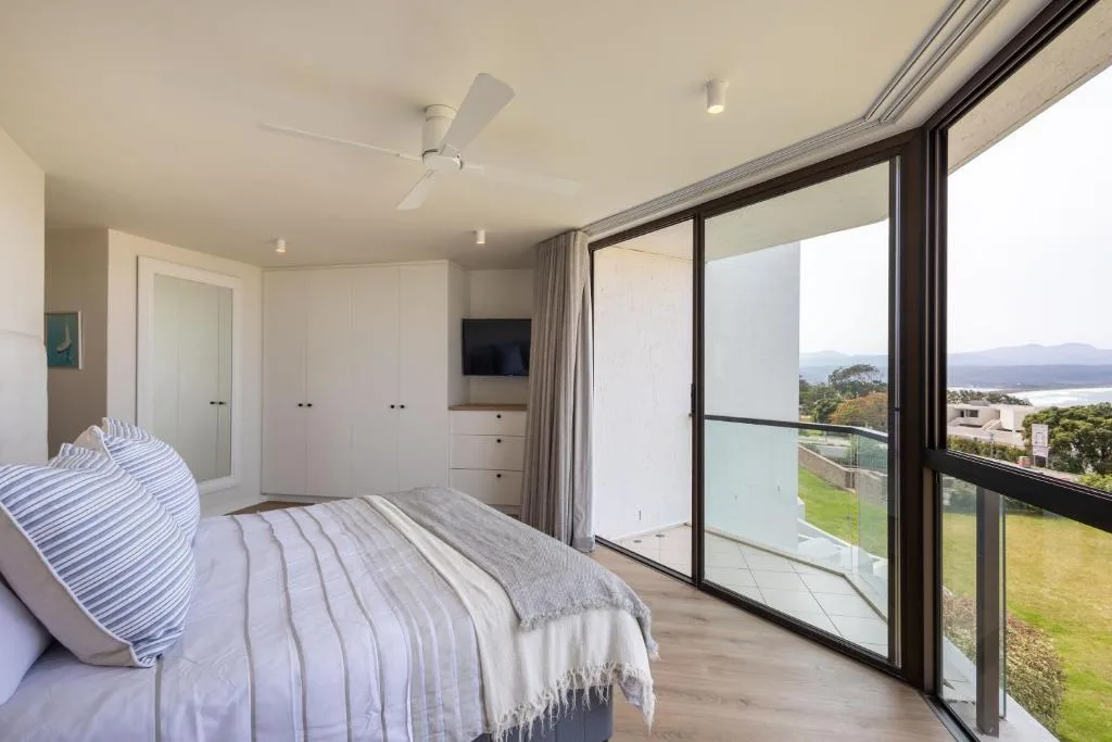 Modern bedroom with built-in wardrobes, sliding glass doors opening to scenic lagoon views