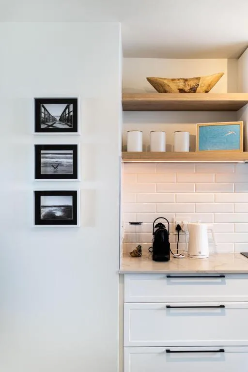 Modern kitchen nook with open shelving, decorative items, and framed coastal artwork