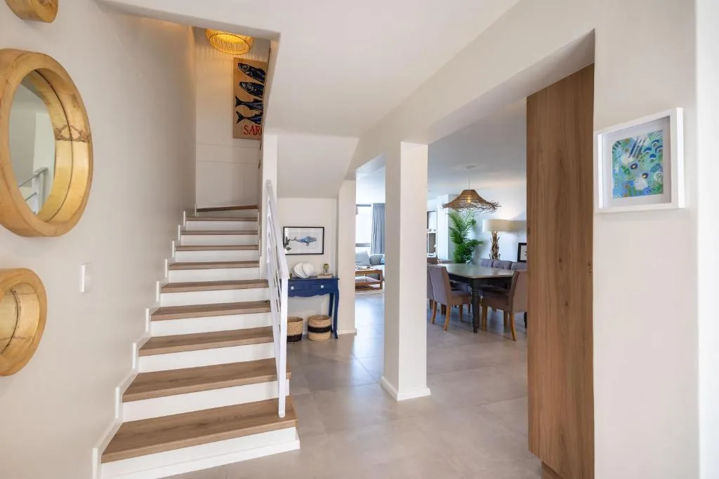Modern interior hallway with wooden staircase, coastal artwork, and dining area view