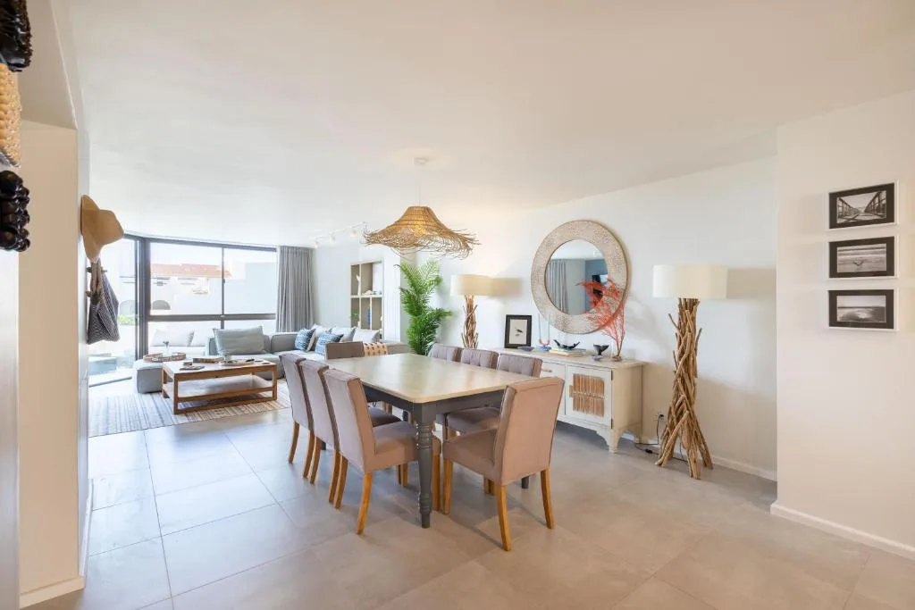 Open-plan dining area with wooden table and upholstered chairs, lounge visible beyond