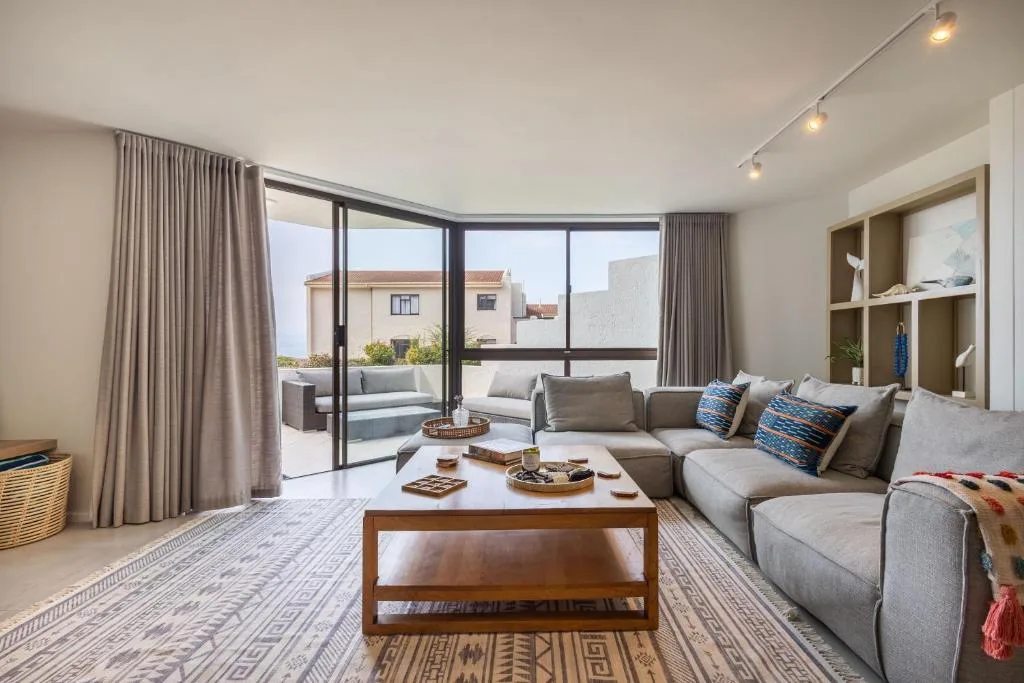 Modern lounge with gray sofa, wooden coffee table, and ocean view through glass doors