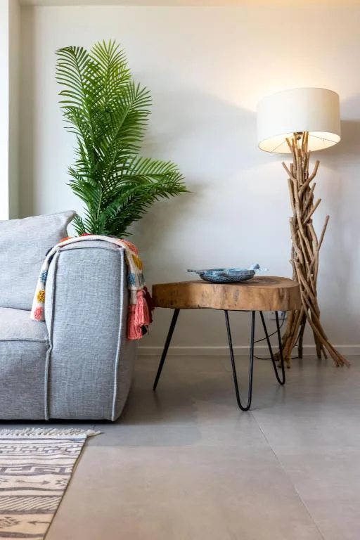 Modern lounge corner with gray sofa, potted palm plant, and driftwood floor lamp