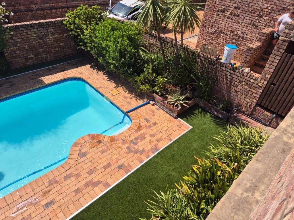 Bright turquoise swimming pool with brick paving and manicured garden surroundings