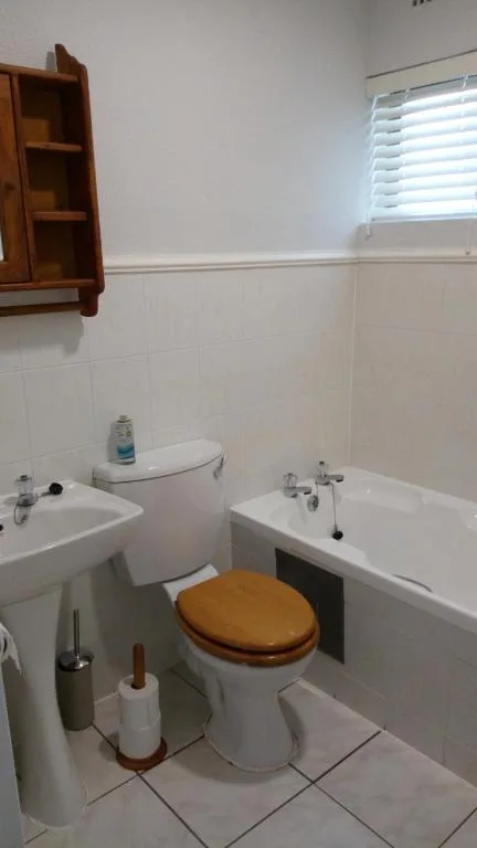 Clean bathroom with toilet, sink, bathtub and wooden wall cabinet