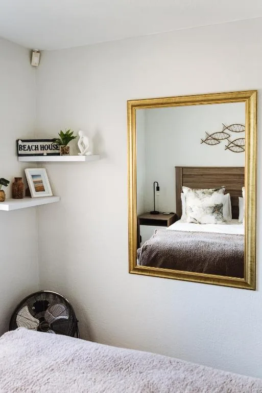 Cozy bedroom corner with bed, gold mirror, and coastal decor shelving