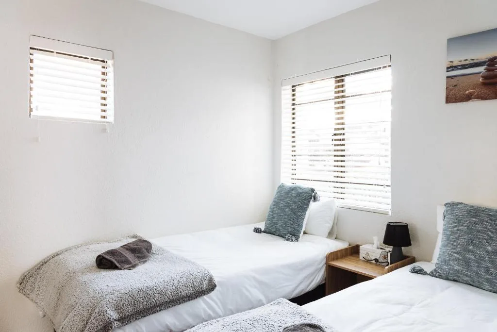 Bright bedroom with two single beds and teal cushions, natural light from windows