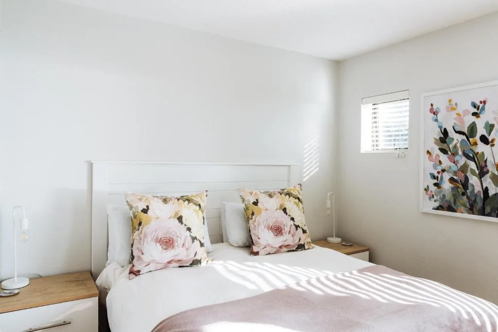 Bright bedroom with white bedframe and floral accent pillows