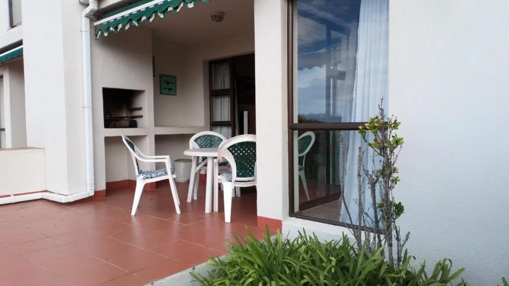 Covered patio with white chairs and small table, terracotta floor
