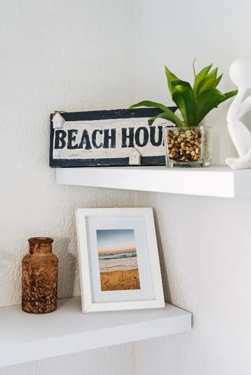 Decorative shelf with beach house sign, framed ocean photo, plant, and bottles