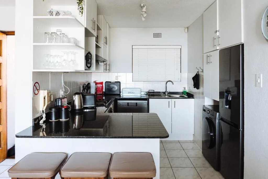 Modern white kitchen with black countertops, stainless steel appliances, and open shelving
