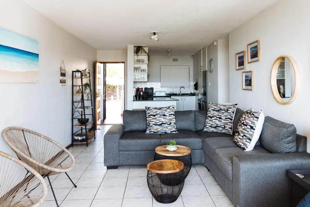 Modern lounge with gray sofa, woven accent chair, and open-plan kitchen view